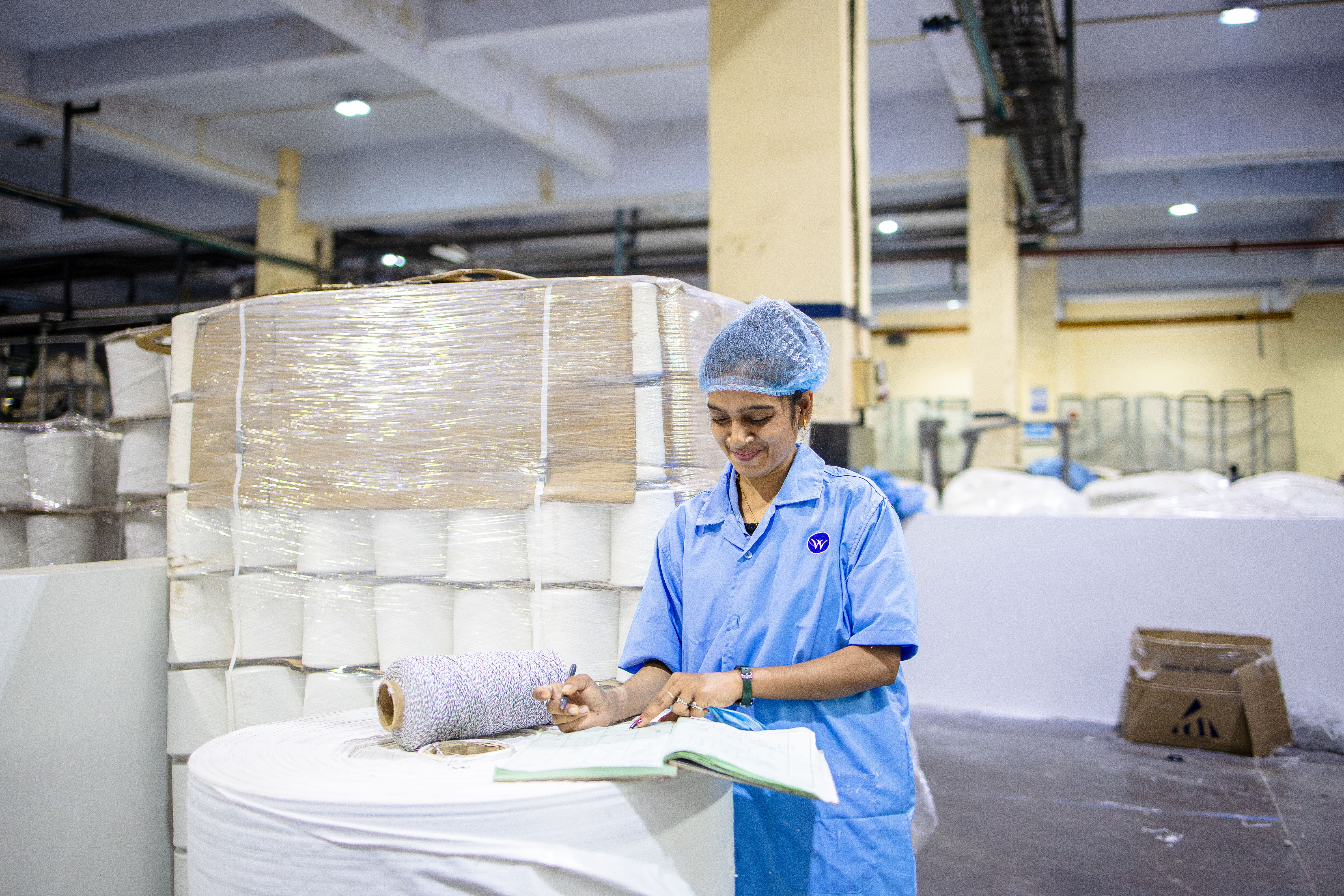 A stores worker updating a paper register beside stacked yarn cones